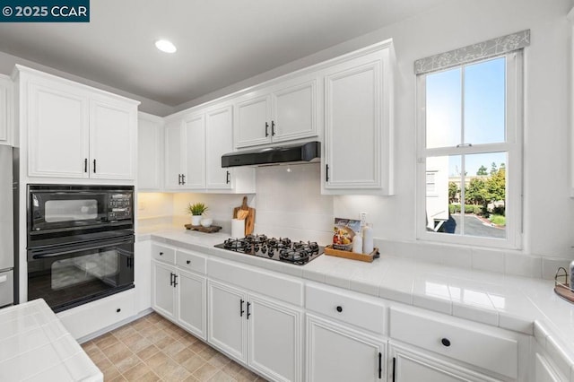 kitchen with black appliances, tile countertops, white cabinetry, and plenty of natural light