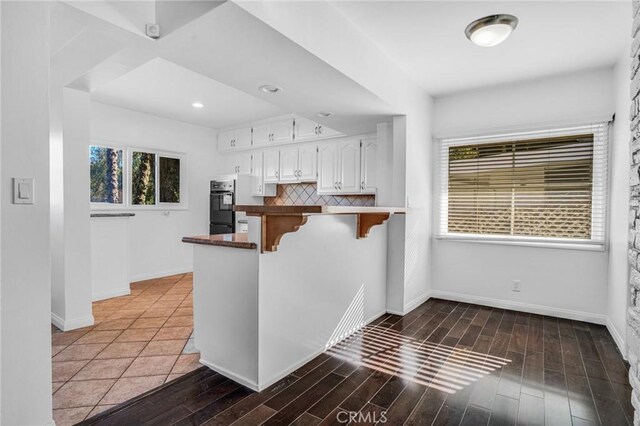 kitchen featuring black double oven, white cabinetry, tasteful backsplash, kitchen peninsula, and a breakfast bar