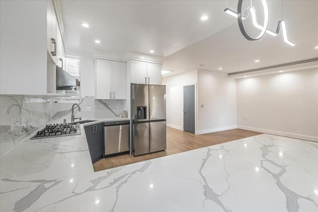 kitchen featuring hanging light fixtures, sink, white cabinets, light stone counters, and stainless steel appliances