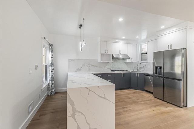 kitchen featuring white cabinets, decorative light fixtures, backsplash, stainless steel appliances, and light stone counters