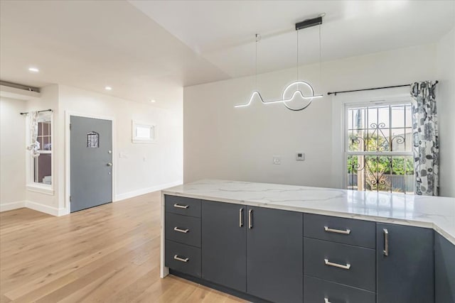 kitchen featuring decorative light fixtures, light hardwood / wood-style floors, and light stone counters