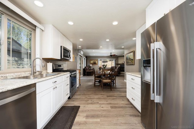 kitchen featuring light stone countertops, white cabinetry, sink, light wood-type flooring, and stainless steel appliances