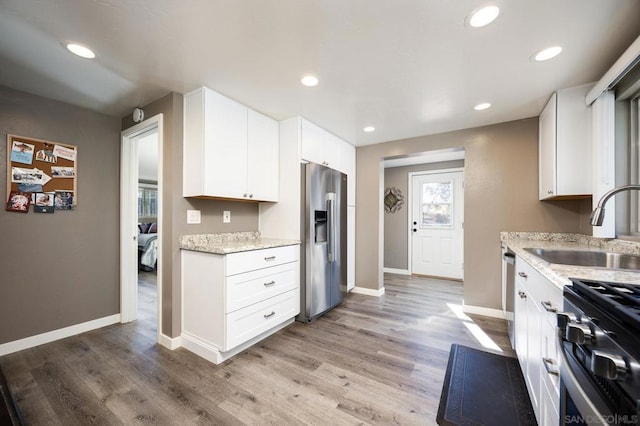 kitchen with light hardwood / wood-style floors, light stone countertops, appliances with stainless steel finishes, white cabinetry, and sink