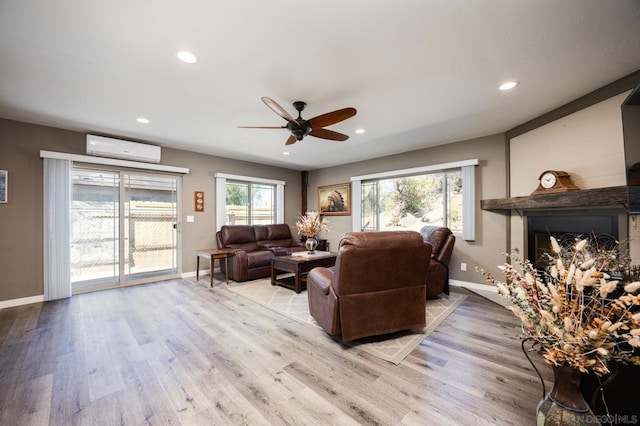 living room with ceiling fan, an AC wall unit, and light hardwood / wood-style flooring