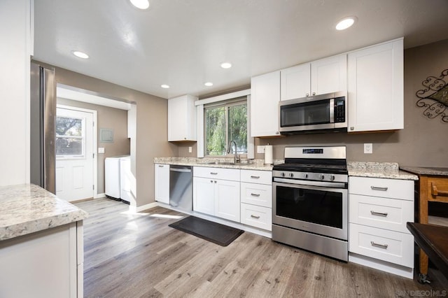 kitchen with separate washer and dryer, appliances with stainless steel finishes, white cabinetry, sink, and light wood-type flooring