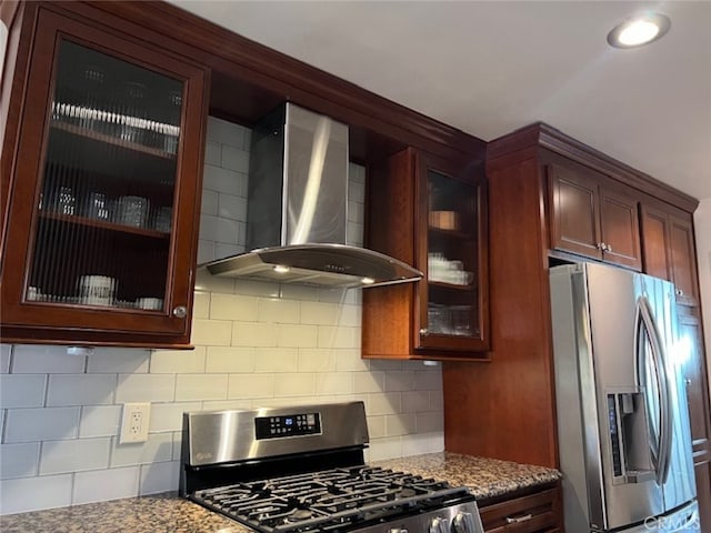 kitchen featuring backsplash, stainless steel appliances, dark stone countertops, and wall chimney range hood