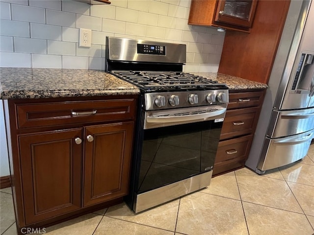 kitchen with tasteful backsplash, light tile patterned floors, dark stone counters, and appliances with stainless steel finishes