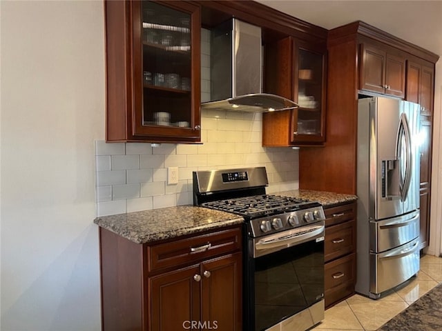 kitchen with dark stone countertops, stainless steel appliances, light tile patterned floors, and wall chimney range hood