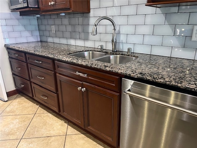 kitchen with sink, light tile patterned floors, appliances with stainless steel finishes, dark stone countertops, and tasteful backsplash