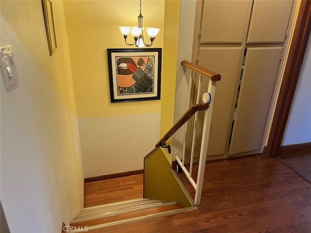 stairway featuring wood-type flooring and an inviting chandelier