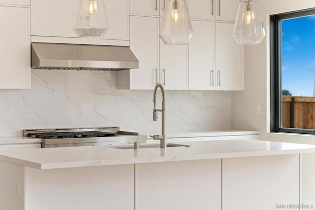 kitchen with wall chimney exhaust hood, backsplash, white cabinetry, and hanging light fixtures