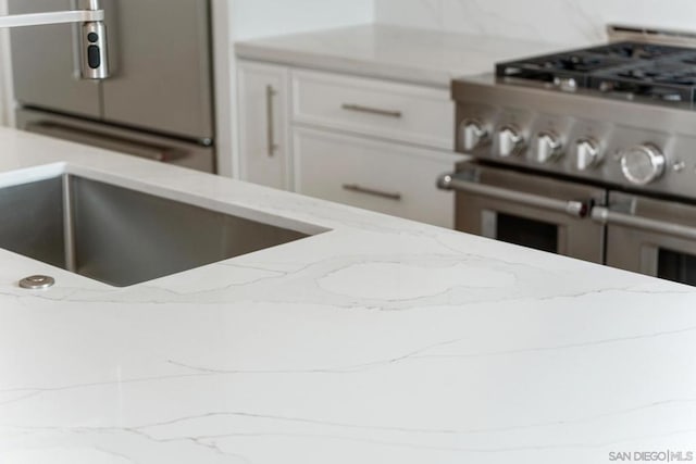 kitchen featuring double oven range, white cabinetry, light stone counters, and fridge