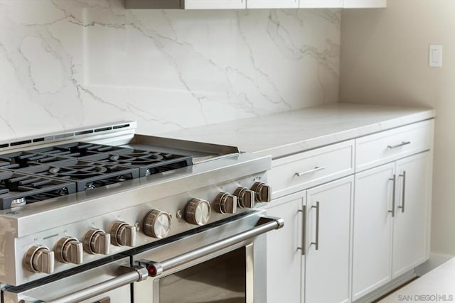 kitchen featuring light stone counters, white cabinets, double oven range, and tasteful backsplash