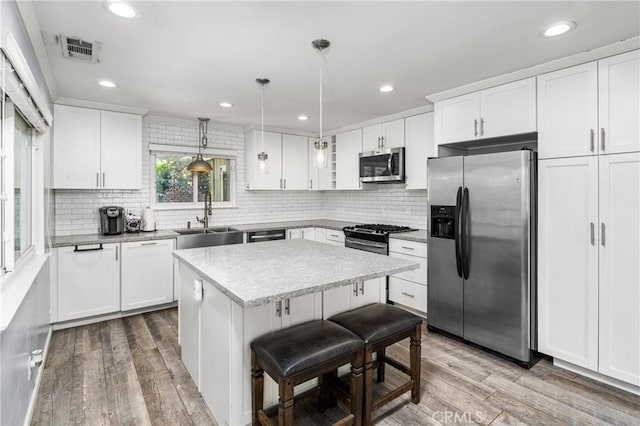 kitchen featuring appliances with stainless steel finishes, sink, decorative light fixtures, white cabinetry, and a center island