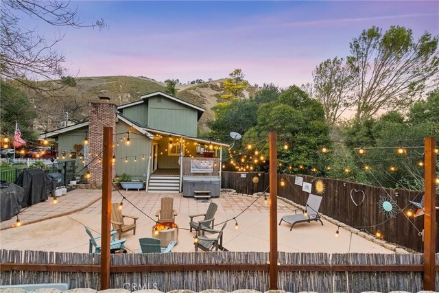 deck at dusk featuring a mountain view, a hot tub, and a patio