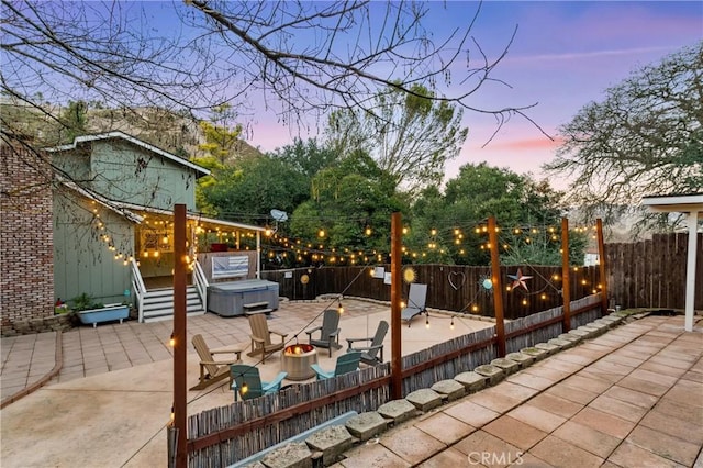 patio terrace at dusk featuring an outdoor fire pit and a hot tub