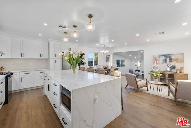 kitchen featuring stainless steel microwave, white cabinets, hanging light fixtures, light stone counters, and gas stove