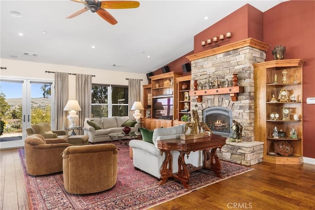 living room featuring hardwood / wood-style flooring, ceiling fan, a stone fireplace, and vaulted ceiling