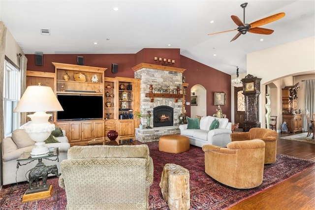 living room with ceiling fan, lofted ceiling, dark hardwood / wood-style floors, and a stone fireplace