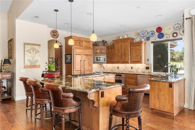 kitchen featuring a kitchen island, built in appliances, hanging light fixtures, and dark stone countertops