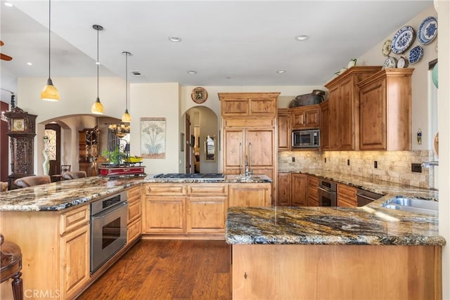 kitchen featuring built in appliances, kitchen peninsula, pendant lighting, dark stone counters, and backsplash