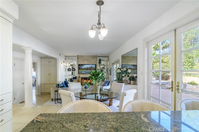 dining area with light tile patterned floors, a large fireplace, a chandelier, and ornate columns