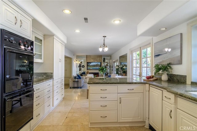 kitchen with black double oven, dark stone counters, decorative light fixtures, and kitchen peninsula