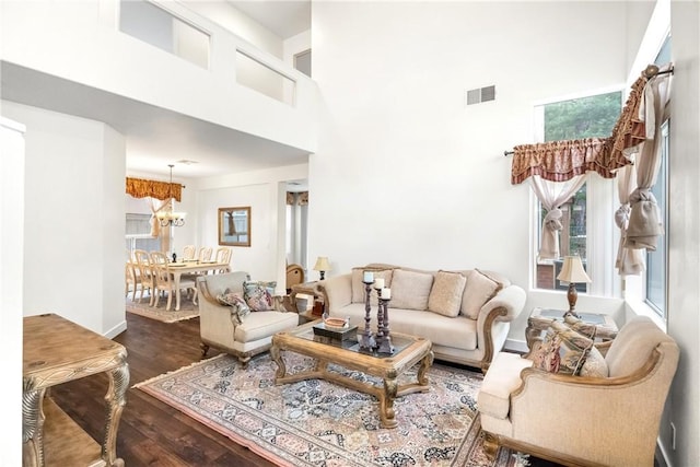 living room with a towering ceiling, a notable chandelier, and dark hardwood / wood-style flooring