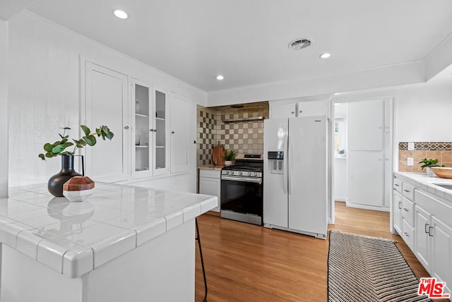 kitchen with stainless steel range with gas stovetop, white cabinets, tasteful backsplash, white fridge with ice dispenser, and tile countertops