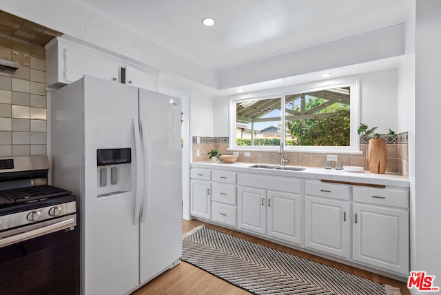 kitchen featuring white cabinetry, white fridge with ice dispenser, tile countertops, stainless steel gas range, and decorative backsplash