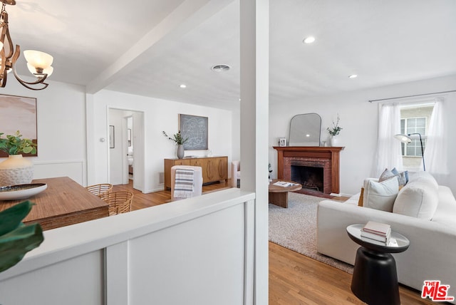 living room featuring a notable chandelier, beamed ceiling, light hardwood / wood-style flooring, and a fireplace