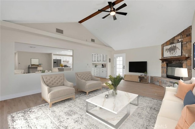 living room featuring hardwood / wood-style floors, a stone fireplace, high vaulted ceiling, ceiling fan, and beam ceiling