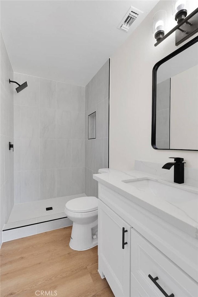 bathroom with hardwood / wood-style floors, toilet, vanity, and a tile shower