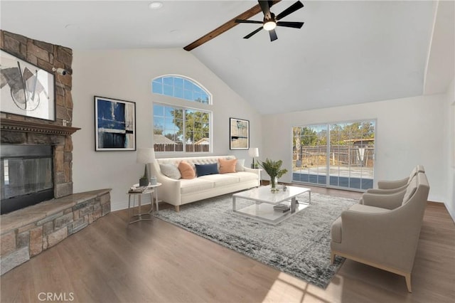 living room with beamed ceiling, hardwood / wood-style floors, plenty of natural light, and a stone fireplace