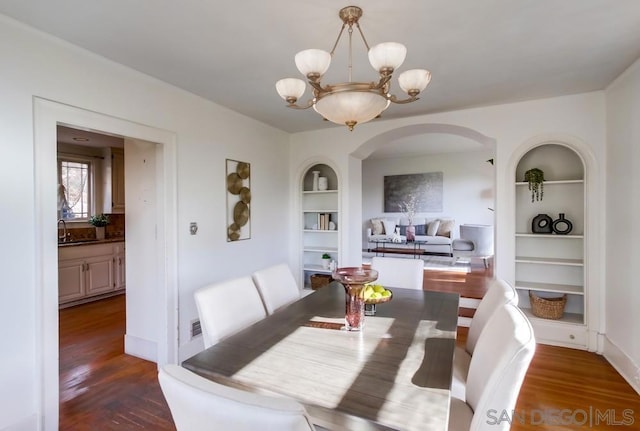 dining space with built in shelves, an inviting chandelier, dark hardwood / wood-style floors, and sink