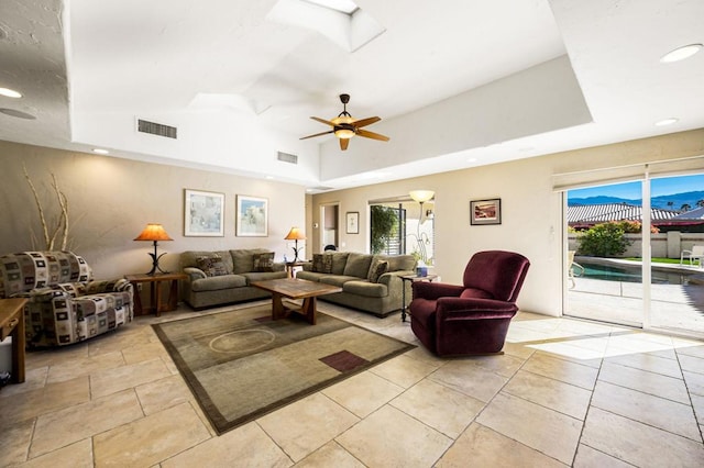 living room featuring ceiling fan, a skylight, and a raised ceiling