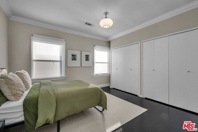 bedroom featuring dark wood-type flooring, two closets, and ornamental molding