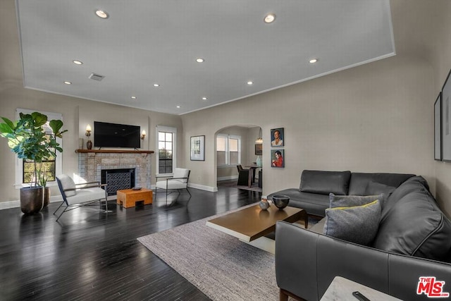 living room with dark hardwood / wood-style floors, a stone fireplace, and ornamental molding