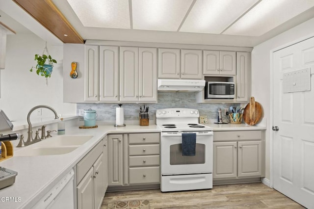 kitchen with sink, white appliances, light wood-type flooring, and tasteful backsplash