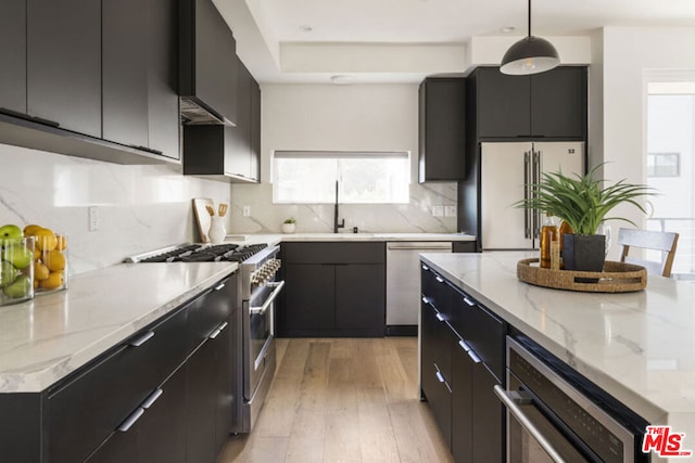 kitchen with hanging light fixtures, appliances with stainless steel finishes, sink, light hardwood / wood-style floors, and decorative backsplash