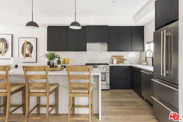 kitchen with a kitchen breakfast bar, hanging light fixtures, high quality appliances, backsplash, and light wood-type flooring