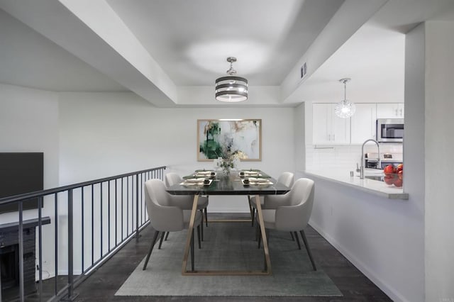 dining area featuring sink, dark wood-type flooring, and a tray ceiling