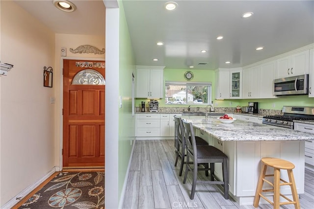 kitchen with white cabinets, a center island, a kitchen bar, stainless steel appliances, and light stone counters