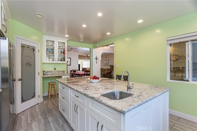 kitchen featuring light stone countertops, white cabinetry, sink, stainless steel fridge, and a center island with sink