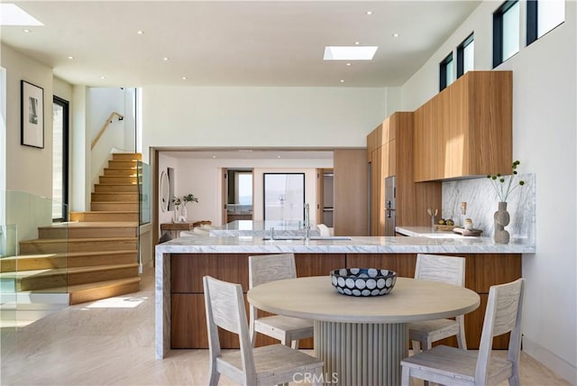 kitchen featuring a kitchen bar, a skylight, sink, kitchen peninsula, and light tile patterned floors