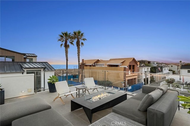 patio terrace at dusk featuring a balcony, a water view, and a fire pit