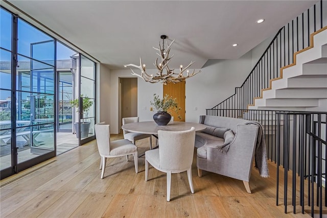 dining space featuring a wall of windows, a notable chandelier, and light wood-type flooring