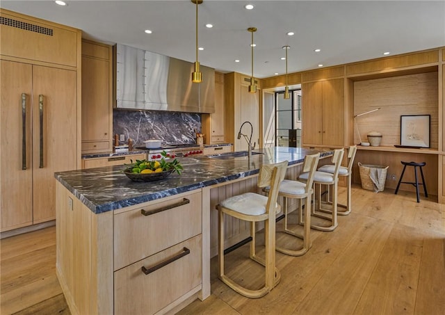 kitchen featuring pendant lighting, light hardwood / wood-style flooring, a kitchen island with sink, and dark stone counters