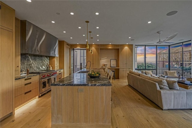 kitchen featuring a spacious island, wall chimney exhaust hood, range with two ovens, tasteful backsplash, and hanging light fixtures