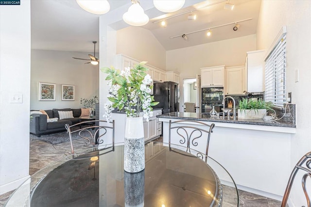 kitchen featuring ceiling fan, dark stone countertops, high vaulted ceiling, tasteful backsplash, and kitchen peninsula